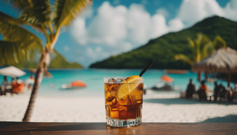 Ein Glas Rum Cocktail am Strand mit Meer und Berge im Hintergrund.