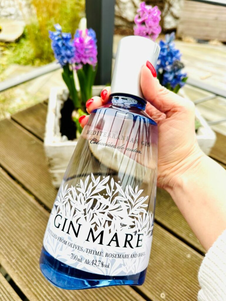 Schrödinger's Katzen Gin: Wo Wissenschaft und Genuss verschmelzen 7 Eine Flasche Gin Mare, im Hintergrund ein Kasten mit Blumen.